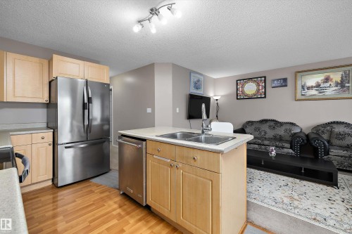 Stainless steel refrigerator, stainless steel dishwasher, light wood-finish cabinetry, kitchen island with dual basin sink, track lighting - 3114 32 Avenue Nw, Edmonton, AB 