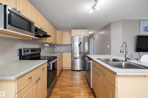 Kitchen featuring stainless steel appliances, light wood-finish cabinetry, a double basin sink, and wood-finish flooring - 3114 32 Avenue Nw, Edmonton, AB 