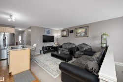 Open-concept living area with a kitchen island featuring an integrated sink, stainless steel appliances, and wood-finish flooring - 