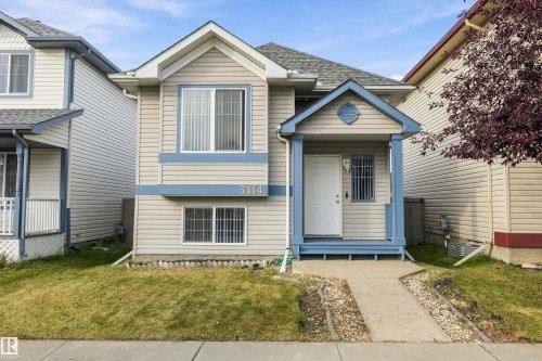 Split-level residence featuring light-colored siding, a blue-trimmed covered front porch, and a concrete walkway - 3114 32 Avenue Nw, Edmonton, AB 