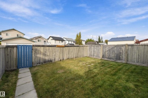 Expansive backyard featuring a manicured lawn, full wood fencing, and a stone-paver pathway leading to a blue wooden gate - 3114 32 Avenue Nw, Edmonton, AB 