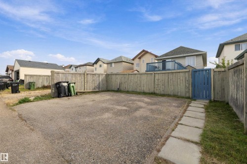Gravel parking area featuring a privacy fence and a paved walkway with a blue gate - 3114 32 Avenue Nw, Edmonton, AB 