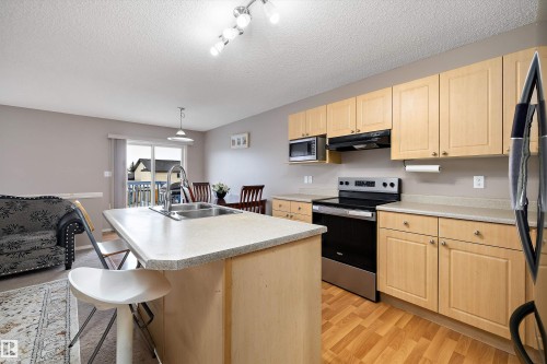 Kitchen island with integrated stainless steel sink, wood-finish cabinetry, stainless steel appliances, wood-finish flooring, and sliding glass door - 3114 32 Avenue Nw, Edmonton, AB 