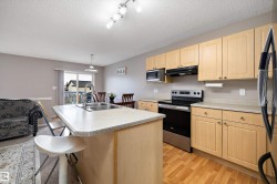 Kitchen island with integrated stainless steel sink, wood-finish cabinetry, stainless steel appliances, wood-finish flooring, and sliding glass door - 