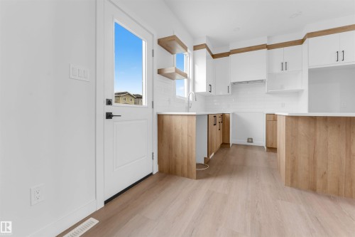 Modern kitchen featuring wood-finish flooring, white cabinetry, wood-tone base cabinetry, white subway tile backsplash, and open shelving - 523 Robinson Blvd, Leduc, AB 