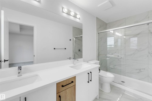 Dual vanity with integrated sinks and chrome fixtures, white countertops, and a full-width mirror - 523 Robinson Blvd, Leduc, AB 