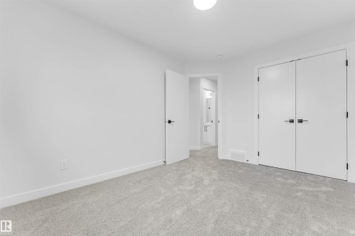 Wall-to-wall carpeting, bright white walls, flush-mount ceiling light, and white interior doors with dark hardware - 523 Robinson Blvd, Leduc, AB 
