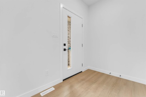 White entry door with a rectangular frosted glass insert, wood-finish flooring, and crisp white walls - 523 Robinson Blvd, Leduc, AB 