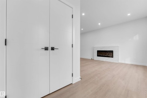 Recessed lighting, wood-finish flooring, electric fireplace with stone-look surround, white interior doors with dark hardware - 523 Robinson Blvd, Leduc, AB 