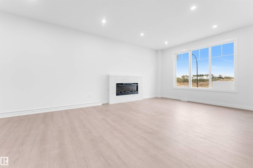 Expansive room featuring wood-finish flooring, recessed lighting, a modern fireplace with a light-toned surround, and large windows - 523 Robinson Blvd, Leduc, AB 