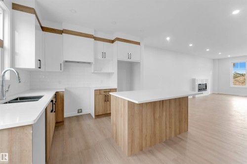 Modern kitchen featuring white shaker cabinets, wood-finish lower cabinetry, white subway tile backsplash, a stainless steel sink, and light wood-finish flooring - 523 Robinson Blvd, Leduc, AB 