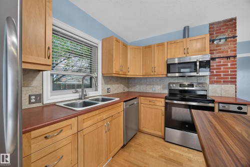 Kitchen featuring wood-finish cabinetry, stainless steel appliances, dual basin sink, and wood-finish flooring - 9615 75 Avenue Nw, Edmonton, AB 