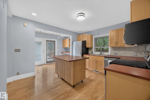 Kitchen featuring wood-finish flooring, natural wood cabinetry, a movable island with wood-finish countertop, stainless steel appliances, and double glass doors - 9615 75 Avenue Nw, Edmonton, AB 