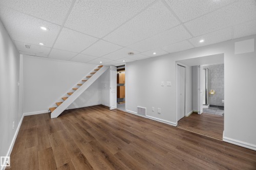 Recessed lighting, wood-finish flooring, white walls, drop ceiling, and a visible staircase - 9615 75 Avenue Nw, Edmonton, AB 