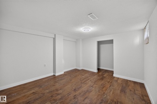Spacious room featuring wood-finish flooring, white walls, and a ceiling-mounted light fixture - 9615 75 Avenue Nw, Edmonton, AB 