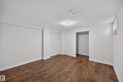 Spacious room featuring wood-finish flooring, white walls, and a ceiling-mounted light fixture - 