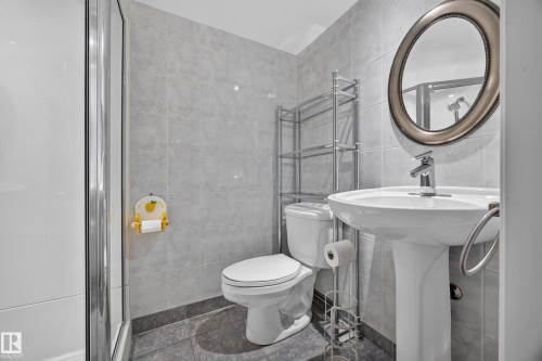 Pedestal sink with chrome faucet, oval mirror, and tiled shower enclosure - 9615 75 Avenue Nw, Edmonton, AB 