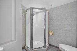 Glass-enclosed corner shower with a polished chrome frame, white shower base, and integrated shelving - 