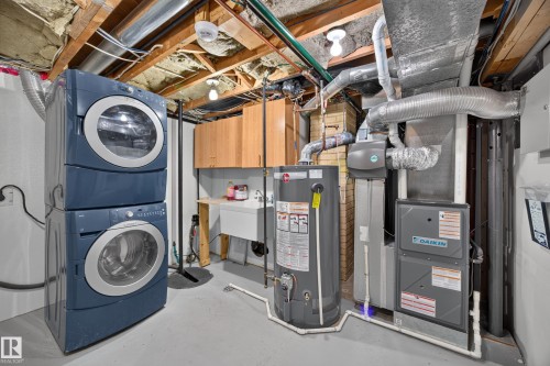 Utility space featuring a stacked washer and dryer, laundry sink, and wood-finish cabinetry - 9615 75 Avenue Nw, Edmonton, AB 