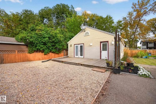 Siding exterior with a gable roof, featuring a wood-finish deck and double glass-panel doors - 9615 75 Avenue Nw, Edmonton, AB 