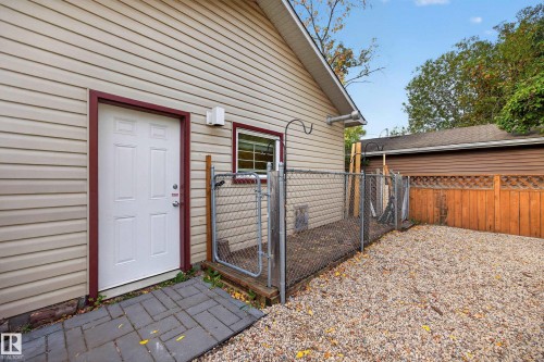 Side entrance featuring a solid white door with red trim, chain-link fencing, and a gravel-covered area - 9615 75 Avenue Nw, Edmonton, AB 