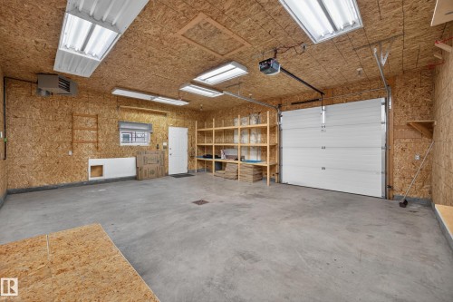 Spacious garage featuring concrete flooring, built-in shelving, overhead lighting, and a white garage door - 9615 75 Avenue Nw, Edmonton, AB 