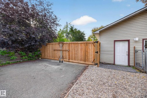Wood privacy fence with rolling gate, gravel parking area, asphalt surface, and exterior siding - 9615 75 Avenue Nw, Edmonton, AB 