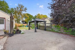 Expansive paved area with a dark metal gazebo, mature trees, and a wooden fence - 