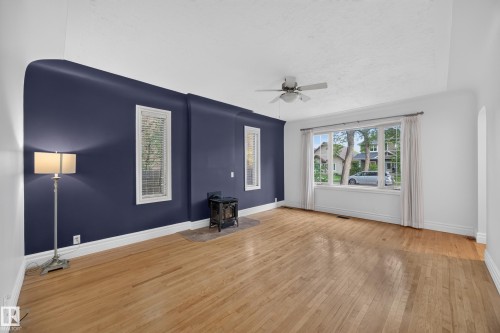 Hardwood flooring, bay window with multiple panes, ceiling fan, freestanding wood-burning stove, and white trim throughout - 9615 75 Avenue Nw, Edmonton, AB 