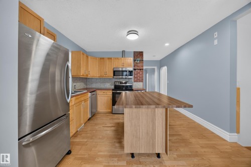 Kitchen featuring stainless steel appliances, wood-finish flooring, light wood cabinetry, a brick accent wall, and a butcher block island - 9615 75 Avenue Nw, Edmonton, AB 