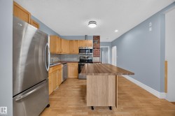 Kitchen featuring stainless steel appliances, wood-finish flooring, light wood cabinetry, a brick accent wall, and a butcher block island - 
