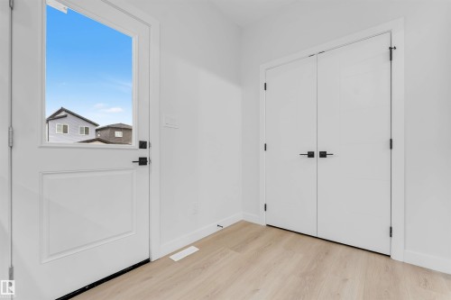 White entry door with upper glass panel, matte black hardware, and wood-finish flooring - 525 Robinson Blvd, Leduc, AB 
