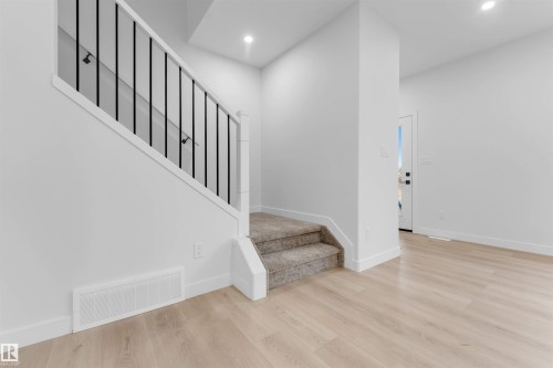 Recessed lighting illuminates the space, featuring light wood-finish flooring and a staircase with carpeted treads and black metal balusters - 525 Robinson Blvd, Leduc, AB 