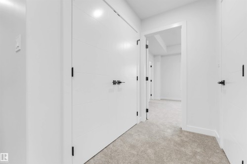 Light-toned carpet flooring, white walls, white doors with horizontal paneling, and matte black hardware - 525 Robinson Blvd, Leduc, AB 