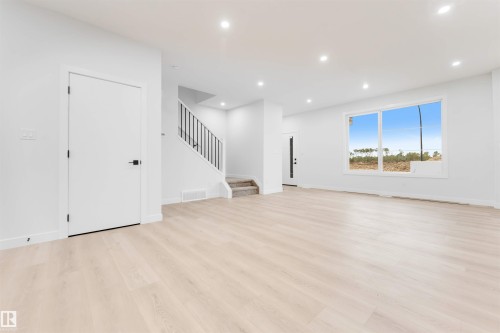Spacious interior with light wood-finish flooring, recessed lighting, and a modern staircase with black metal railings - 525 Robinson Blvd, Leduc, AB 