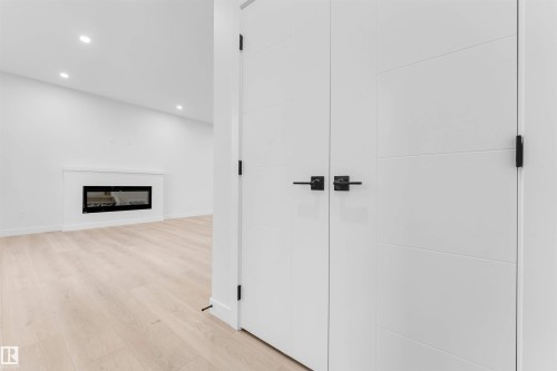 Recessed lighting, wood-finish flooring, white walls, built-in linear fireplace with mantel, and white panel doors with matte black hardware - 525 Robinson Blvd, Leduc, AB 