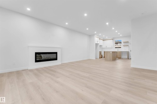 Recessed lighting illuminates the open layout featuring light wood-finish flooring and a contemporary fireplace - 525 Robinson Blvd, Leduc, AB 