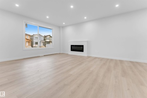 Recessed lighting illuminates the room, featuring light wood-finish flooring and a contemporary fireplace - 525 Robinson Blvd, Leduc, AB 