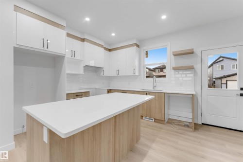 Kitchen featuring a central island with a solid surface countertop, white cabinetry with integrated pulls, wood-finish lower cabinetry, and wood-finish flooring - 525 Robinson Blvd, Leduc, AB 