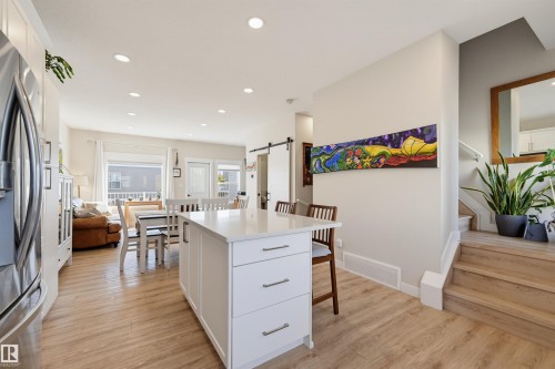 Open-concept living area with wood-finish flooring, recessed lighting, and a white kitchen island featuring a light-toned countertop - #3 150 Everitt Dr N, St. Albert, AB 