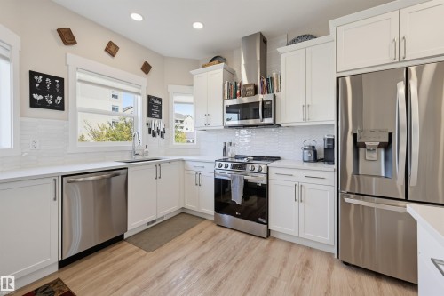 Modern kitchen featuring white shaker cabinetry, stainless steel appliances, light wood-finish flooring, white subway tile backsplash, and recessed lighting - #3 150 Everitt Dr N, St. Albert, AB 