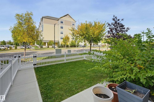 Manicured front yard with a white picket fence, concrete walkway, and mature landscaping - #3 150 Everitt Dr N, St. Albert, AB 
