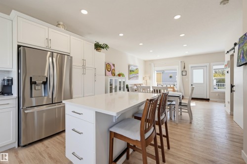Modern kitchen featuring white cabinetry, stainless steel appliances, a center island with countertop seating, recessed lighting, and wood-finish flooring - #3 150 Everitt Dr N, St. Albert, AB 