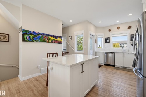 Kitchen featuring a central island with a solid surface countertop, white cabinetry with modern hardware, stainless steel appliances, and wood-finish flooring - #3 150 Everitt Dr N, St. Albert, AB 