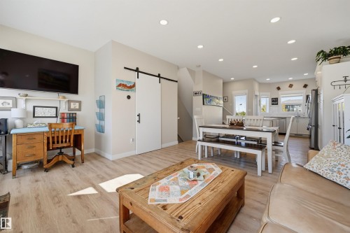Light wood-finish flooring throughout, featuring recessed lighting, a modern barn door, and a kitchen with stainless steel appliances and a tile backsplash - #3 150 Everitt Dr N, St. Albert, AB 