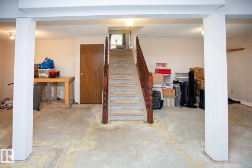 Unfinished concrete flooring, white painted support columns, and a traditional wood staircase - 8 Ash Crescent, St. Albert, AB 