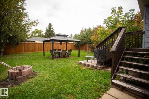 Expansive green space featuring a wooden privacy fence, a multi-level wooden deck, and a brick-built fire pit - 8 Ash Crescent, St. Albert, AB 