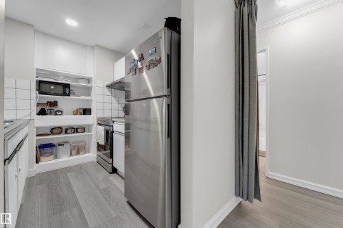 Galley kitchen featuring wood-finish flooring, white subway tile backsplash, stainless steel refrigerator, and integrated open shelving - #113 2508 50 St Nw, Edmonton, AB 