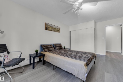 Light wood-finish flooring, built-in closet with sliding doors, ceiling fan, and white painted walls - #113 2508 50 St Nw, Edmonton, AB 