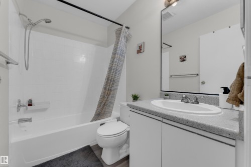 Bathroom with a white vanity featuring a built-in sink, speckled countertop, and wood-finish flooring - #113 2508 50 St Nw, Edmonton, AB 